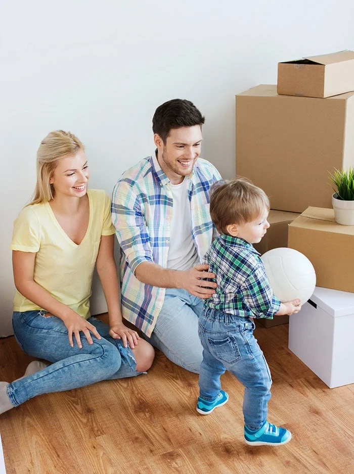 A smiling young mother and father sitting on the hardwood floor of a new home.